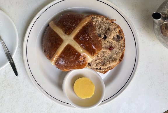 A hot cross bun sliced and served with butter.