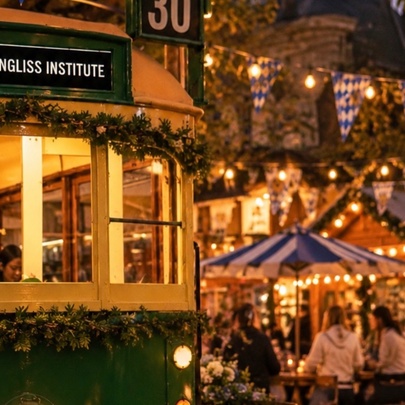 An old W-Class Melbourne Tram with lights and bunting and people wandering around in the background.