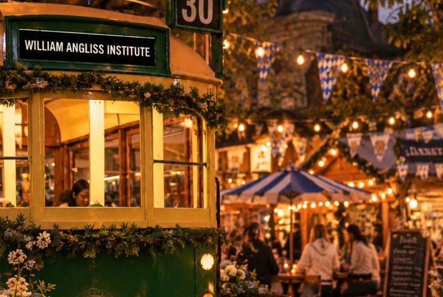 An old W-Class Melbourne Tram with lights and bunting and people wandering around in the background.