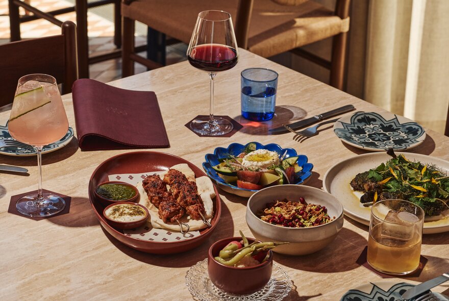 A wooden table at a restaurant with share style plates of Middle Eastern food, beverages, and cutlery.