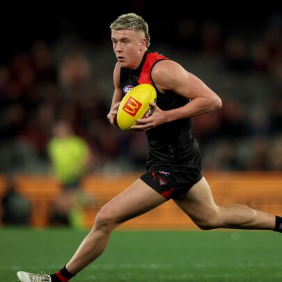 Essendon AFL football player running with the yellow ball during a match.