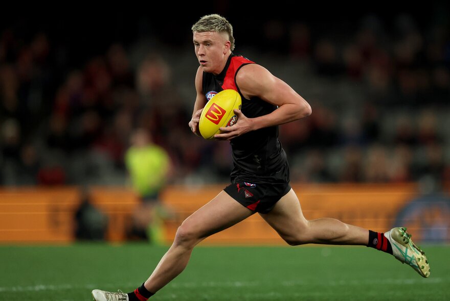 Essendon AFL football player running with the yellow ball during a match.
