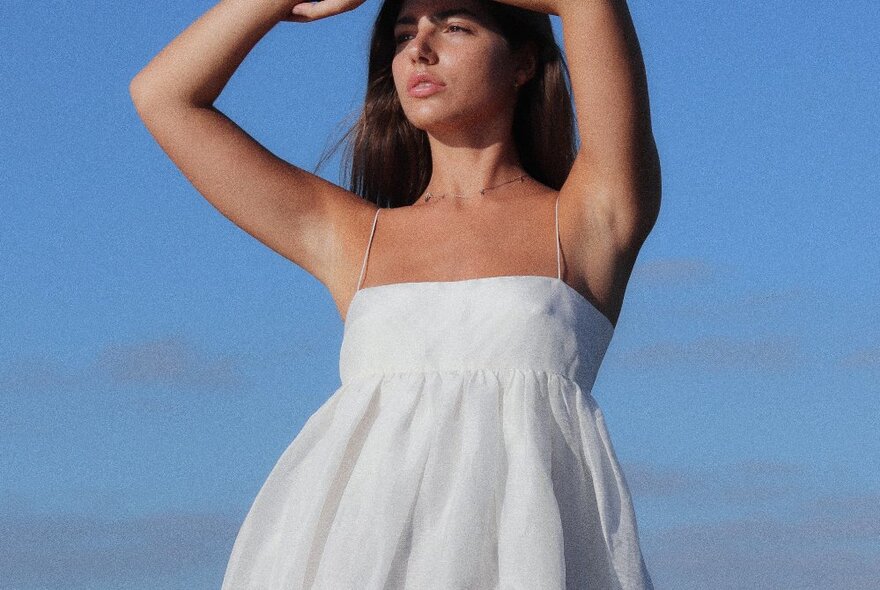 A fashion model with her arms in the air wearing a white dress against a blue background.