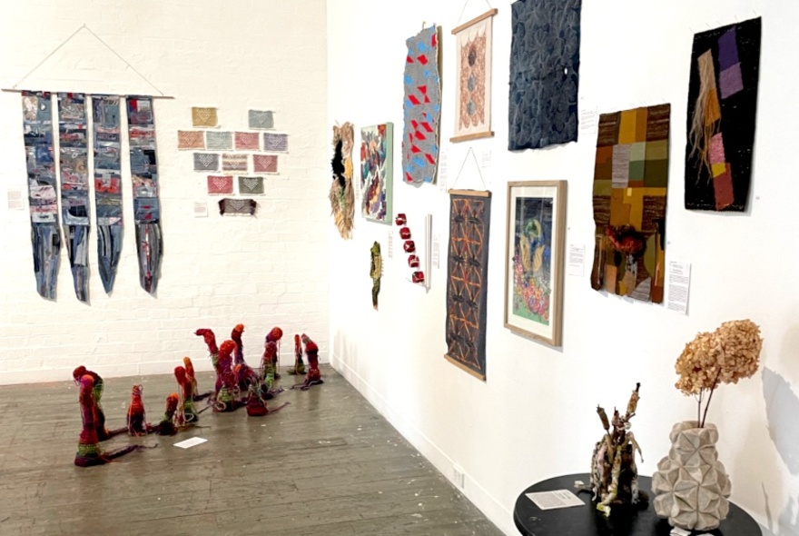 An exhibition of textiles in a gallery setting, arranged on the white walls.