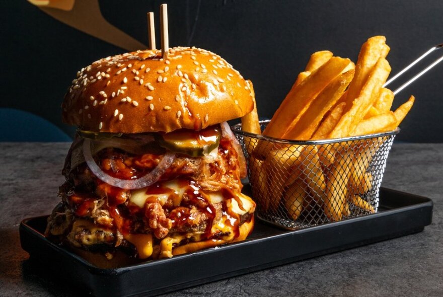 A large hamburger next to a scoop of chips on a tray.