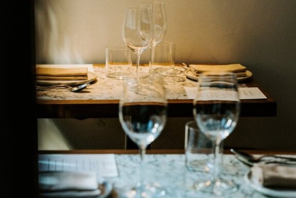 Two empty wine glasses on a table in a dimly lit restaurant, with a second table behind it set for dinner.