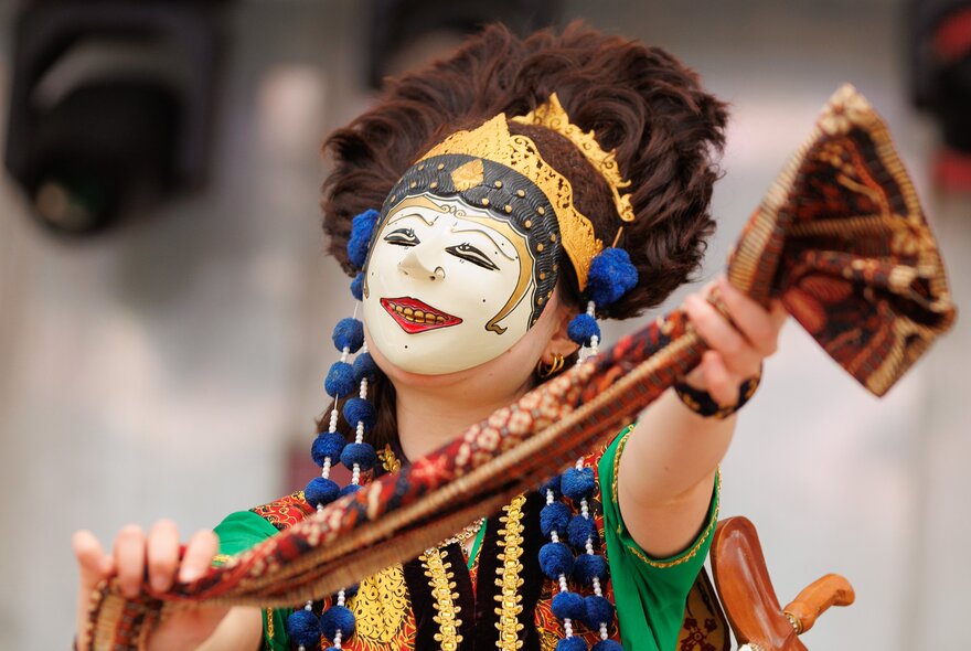 An Indonesian cultural dance performance, with the performer wearing a face mask and headdress and colourful clothing.