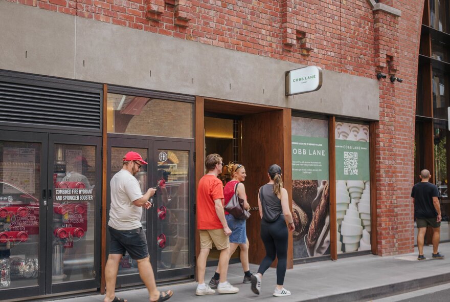 People dressed casually walking past a city bakers. 