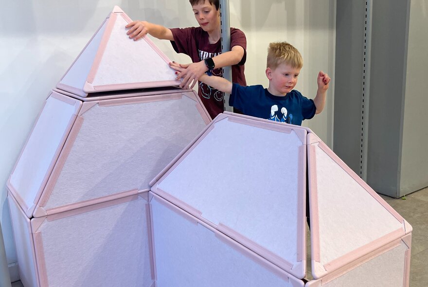 Two kids building cubby houses out of large cardboard panels.