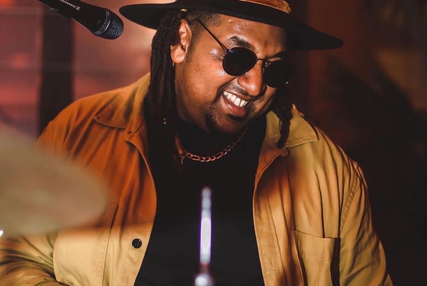 A smiling musician wearing dark glasses playing drums.