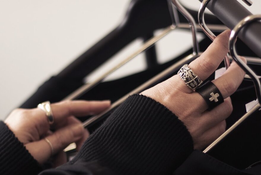 Hands wearing silver goth jewellery and black jumper arranging metal hangers on a rack.