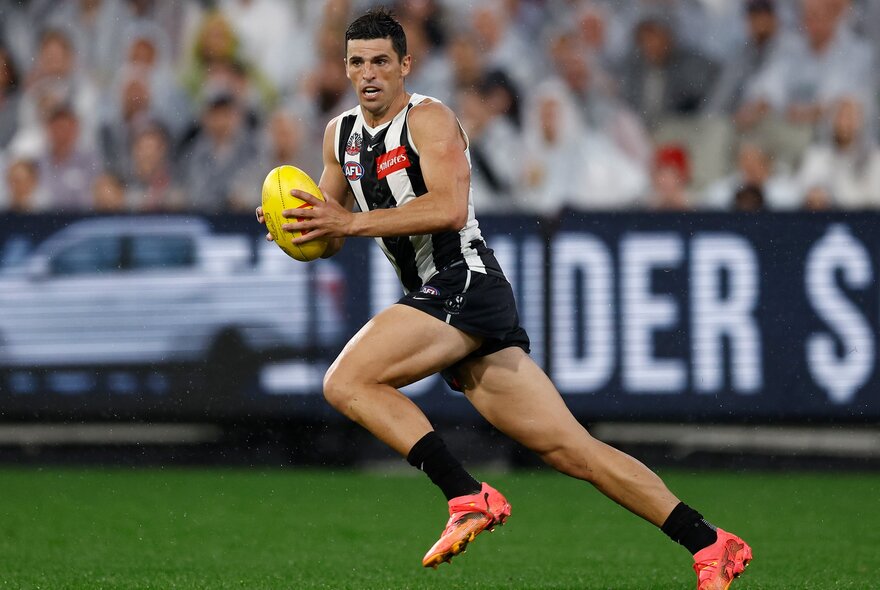 A Collingwood AFL player running with the footy in  his hands.