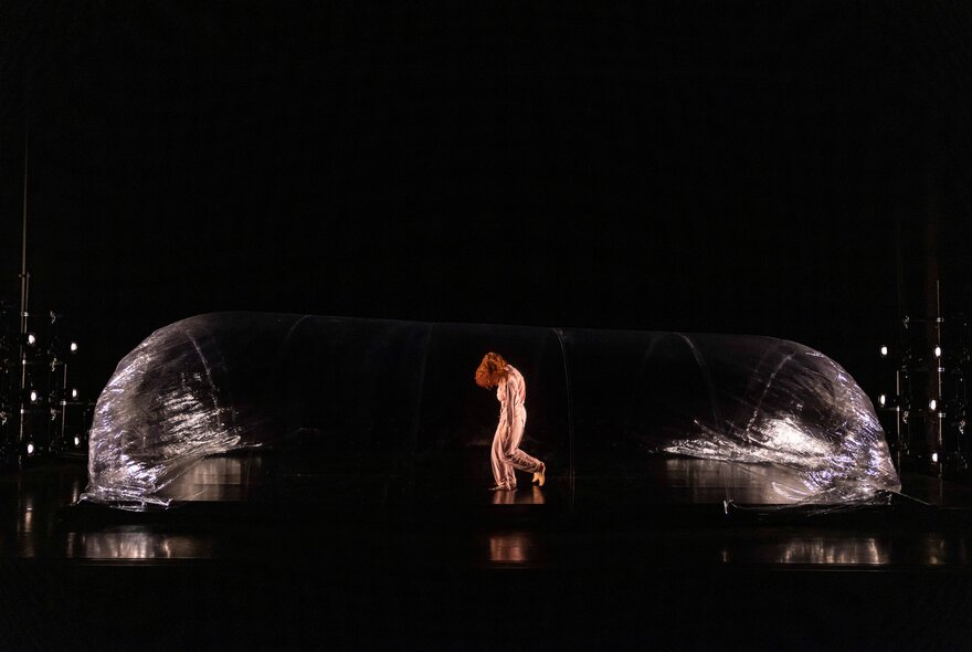 A scene from the contemporary dance work Red by Australian company Dancenorth, with a dancer standing inside a large, transparent, inflatable dome on a dark stage.