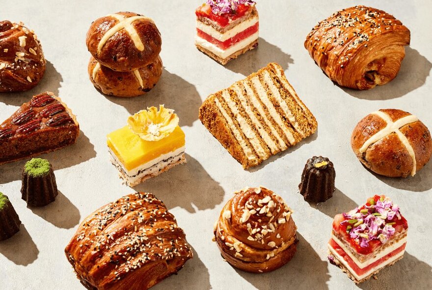 Selection of pastries and cakes including hot cross buns and caneles.