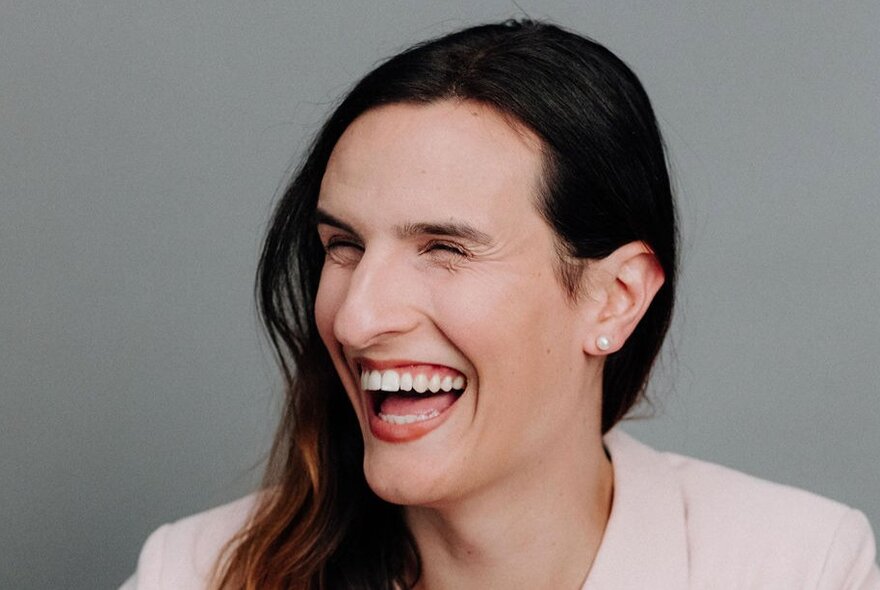 A woman with long dark hair laughing openly to her right. 
