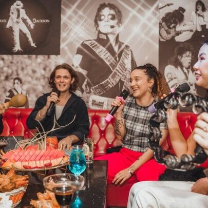 A group of friends singing in a private karaoke room, with the table in front of them filled with platters of food and drinks.