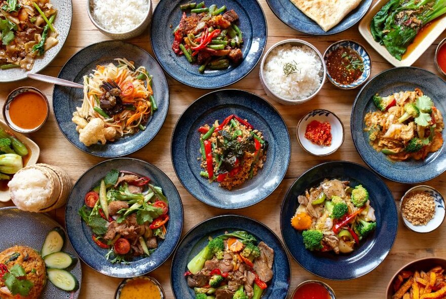 Overhead shot of many dishes of Asian food on a table, with condiments.