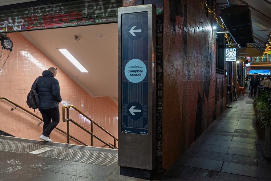 A person walking down the stairs into Campbell Arcade, Degraves Street shops visible on the right. 