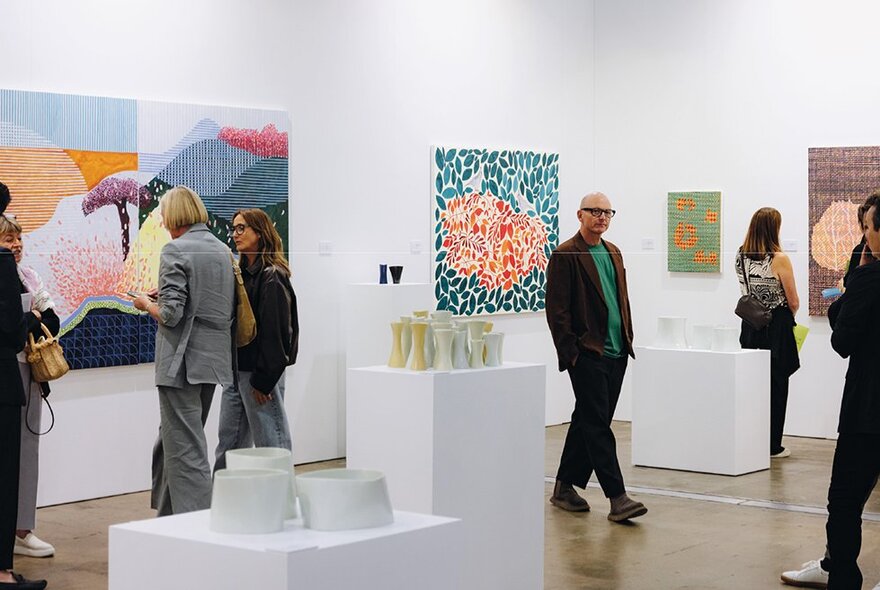 People viewing colourful artworks in a gallery setting.