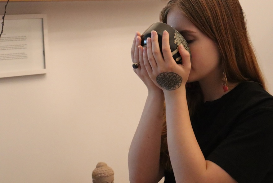 A young woman with a tattoo on her hand drinking traditional Japanese Tea out of a Japanese bowl, with two hands.