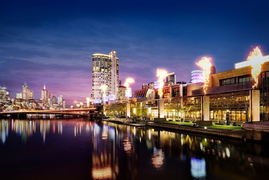 Crown Melbourne building illuminated at night by gas flares and reflections in Yarra River.