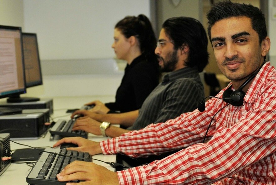 Profile of three people sitting in front of a keyboard and computer screen, with one person facing camera and smiling.