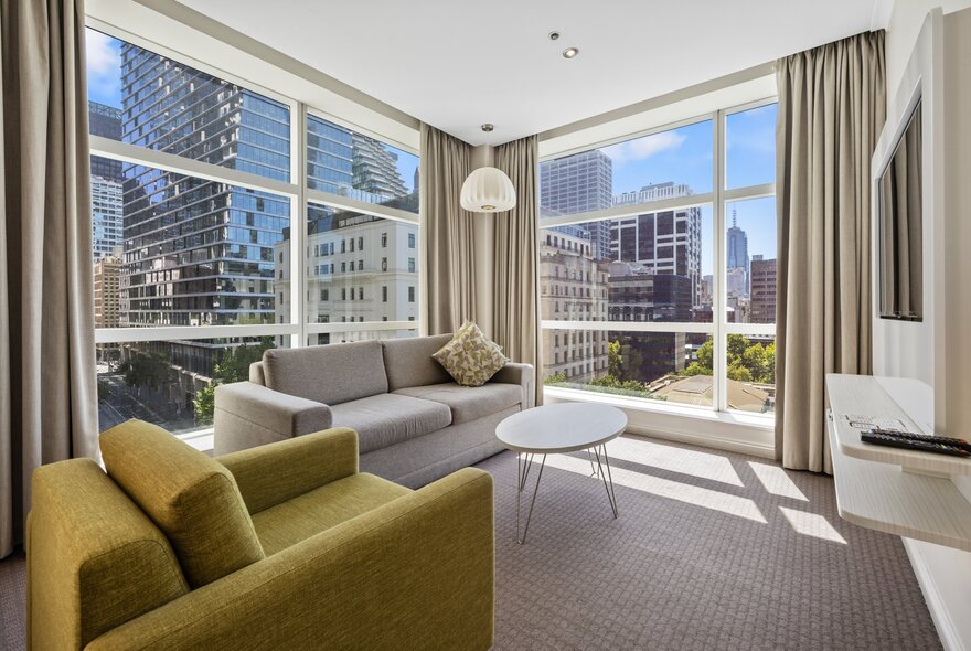 Hotel suite window corner with green and grey seating, city buildings in the background.