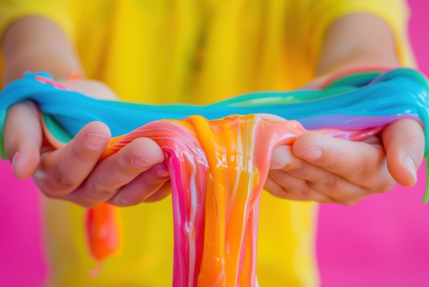 A pair of open outstretched hands holding brightly coloured oozing slime.