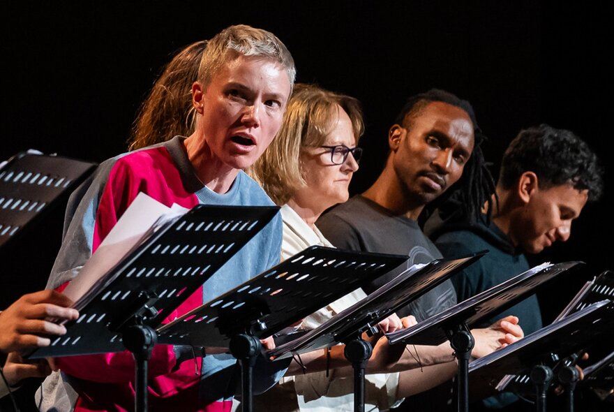 Five actors on stage with pedestal lecturns, conducting a reading of Shakespeare.