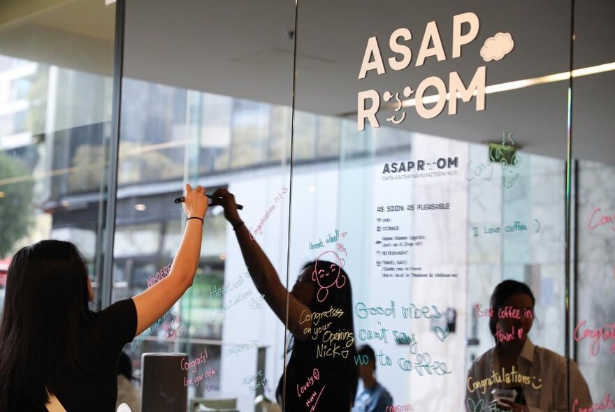 A woman writing menu items on a glass window of a cafe with a paint pen.