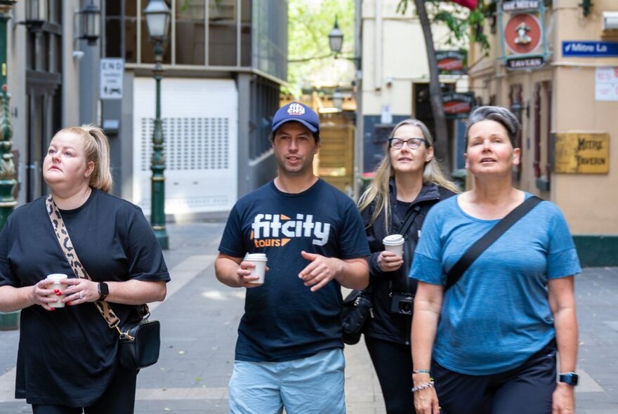 Three people on a walking tour through central Melbourne with a Fit City tour guide, each holding a takeaway coffee.