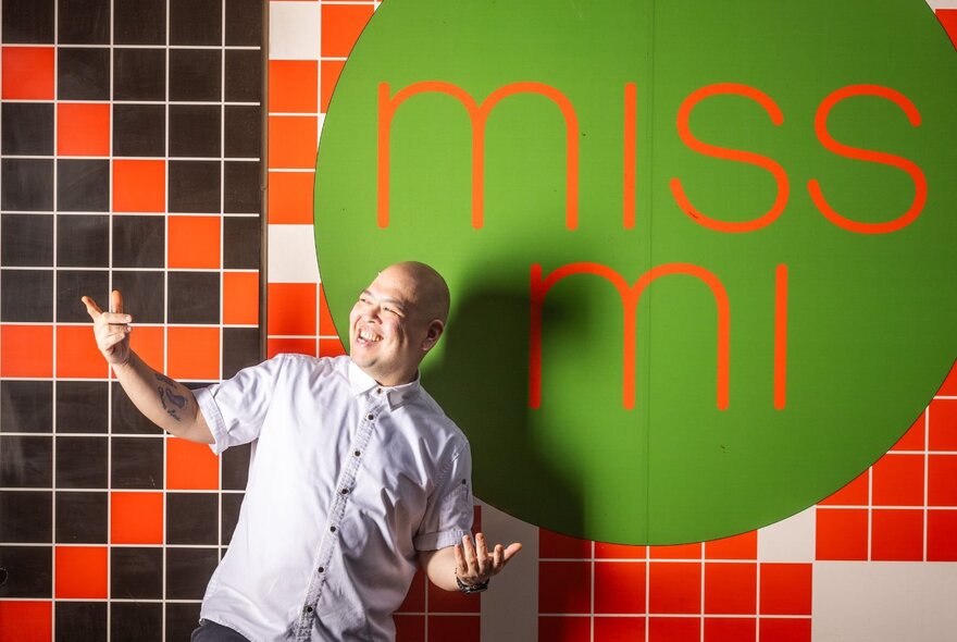 A man smiling and leaning in to a wall with Miss Mi written on it.