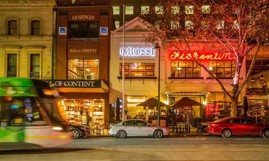 A tram going past three city restaurants with neon signs. 