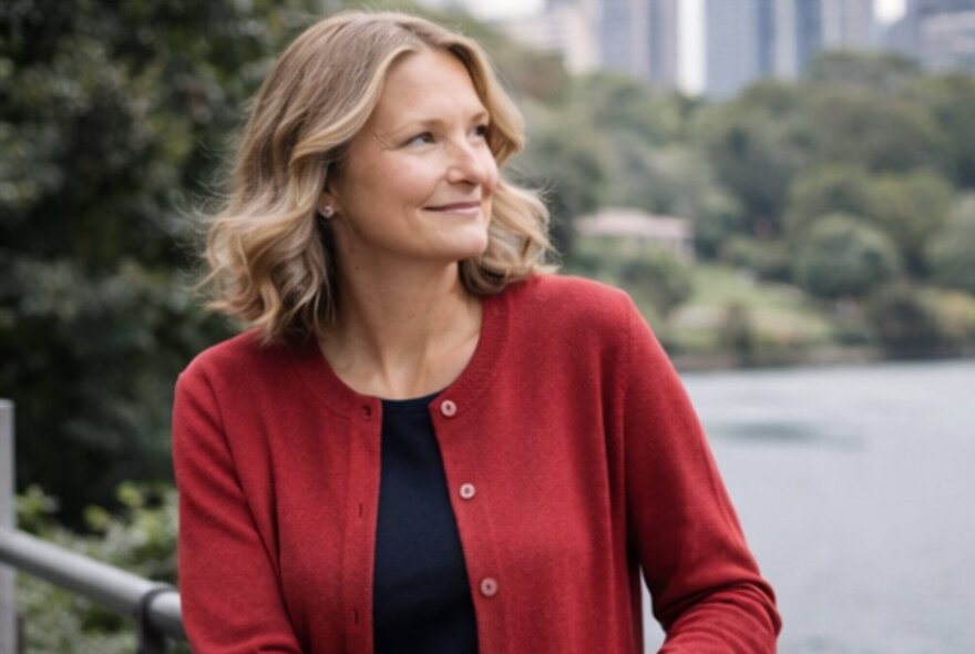 Model wearing an unbuttoned red cardigan in a park setting with city buildings in the background.