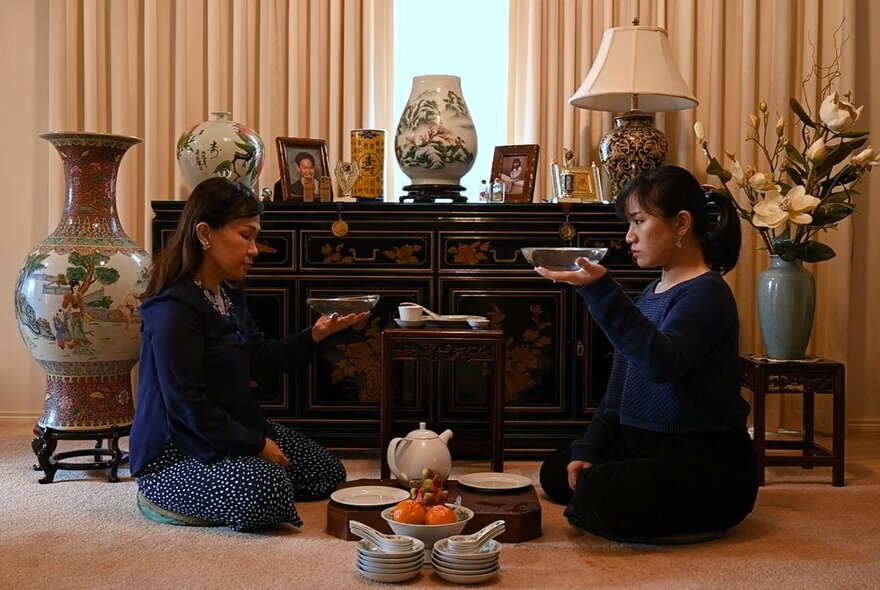 Two women seated on the ground with food and Asian ornaments.
