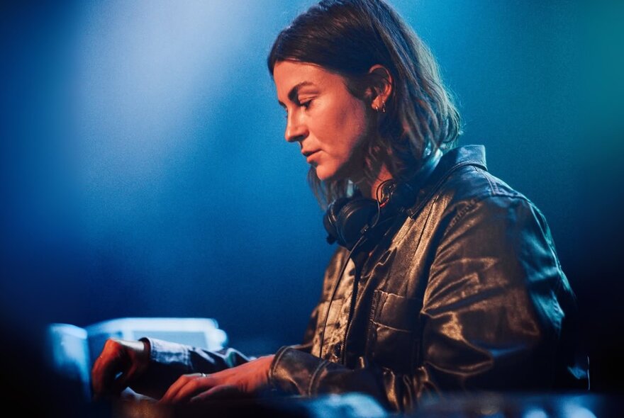 Side-on portrait of a woman with brown hair, looking down as she plays an instrument in front of a dark blue background.