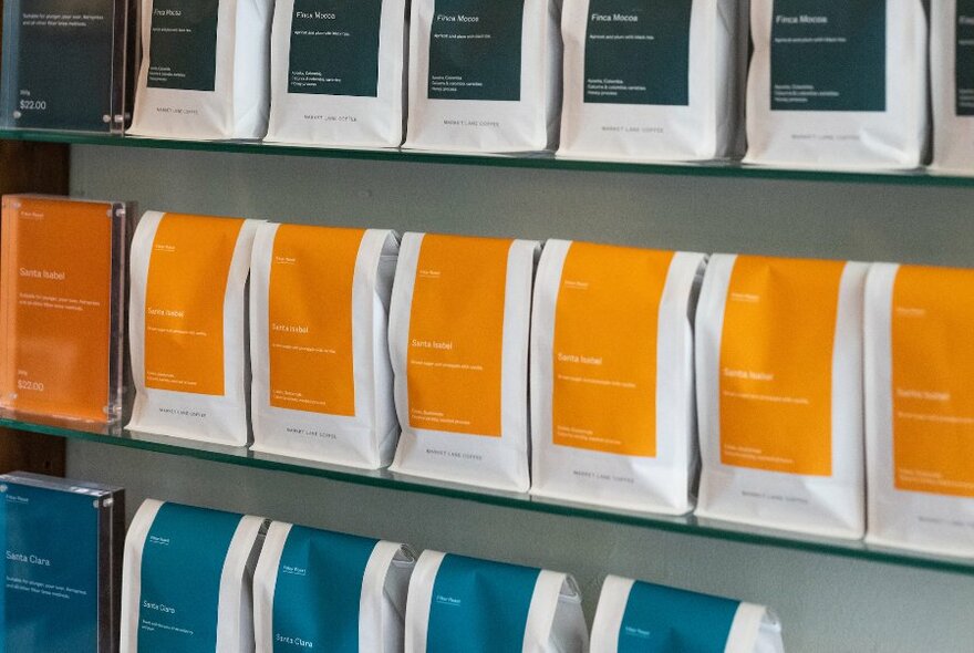 Bags of coffee beans lined up on a glass shelf.