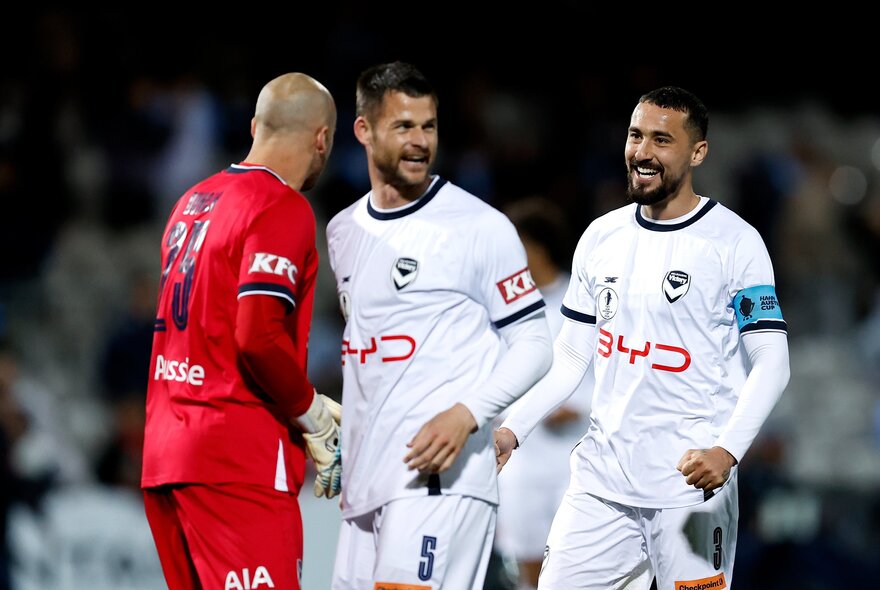 Two Melbourne Victory A-League players talking with a Melbourne City player on the field.