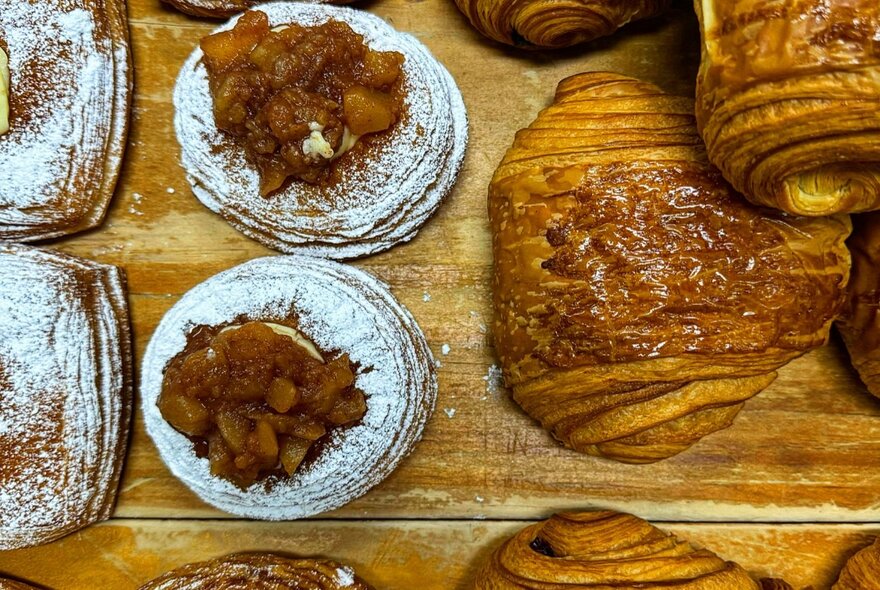 Looking down from above at a selection of pastries and croissants on a wooden board.