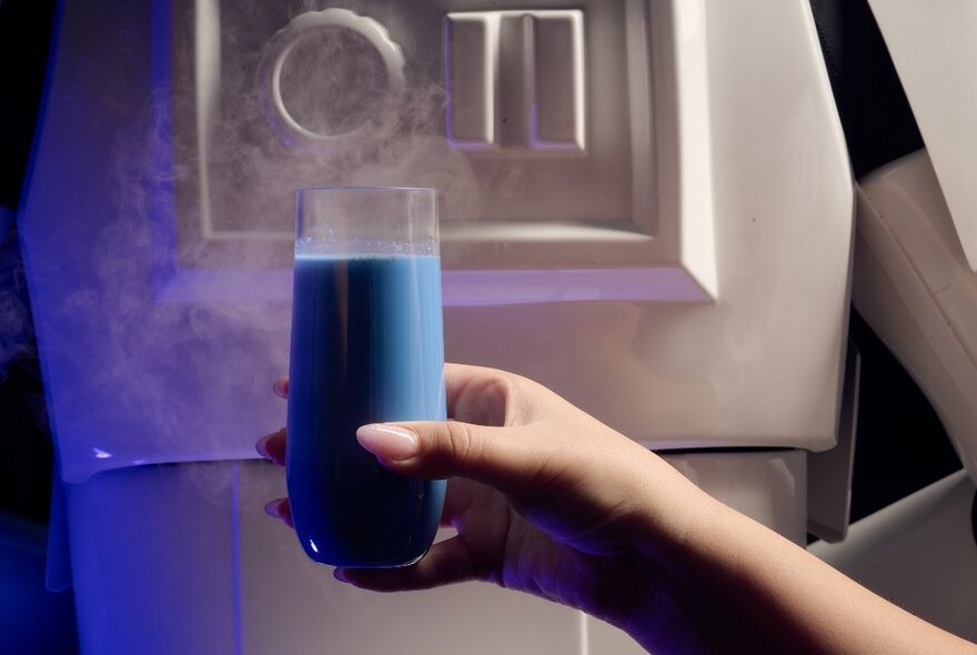A hand holding up glass of blue milk, a white Star Wars Stormtrooper character in the background. 