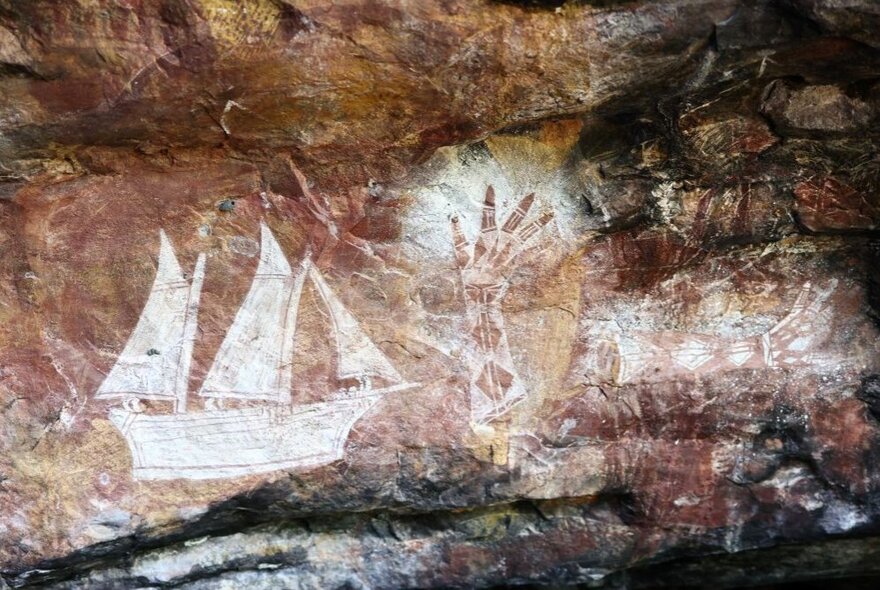 Aboriginal rock art featuring a sailing ship and a hand stencil, on a reddish coloured flat rock surface.