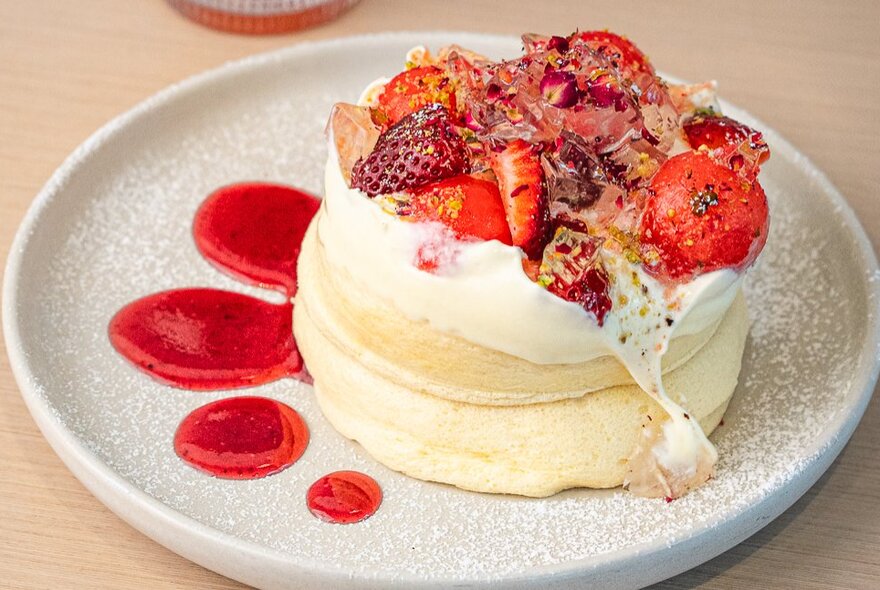 Souffle-style fluffy pancakes topped with strawberries, cream and a dusting of icing sugar.