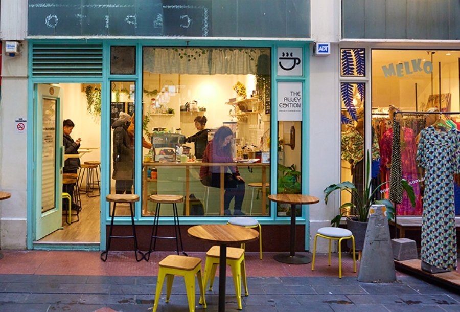 A woman sitting in the window of a blue cafe with seating outside.