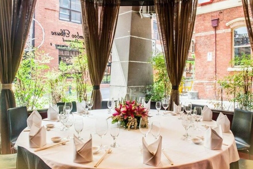 Formal table setting with flowers and napkins against windows with tied curtains.