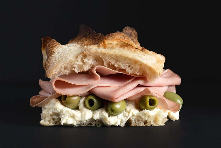 Saluministi panino mortadella sandwich with green olives and creamy cheese in focaccia bread.