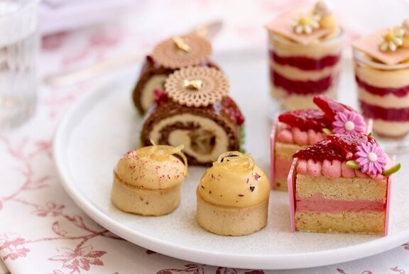 A selection of small desserts and cakes on a white plate as part of a High Tea spread at Langham Hotel's Aria Bar.