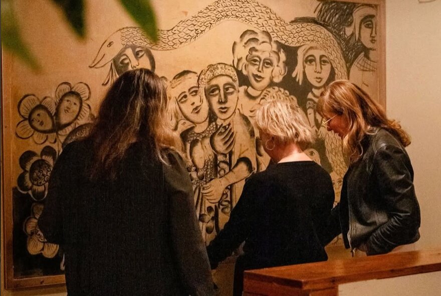 People standing next to a wooden baqr looking at a wall mural of people.