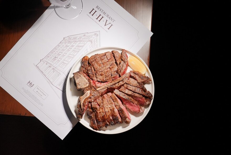 A sliced steak served on a white plate next to a Restaurant 226 menu on a dark table.
