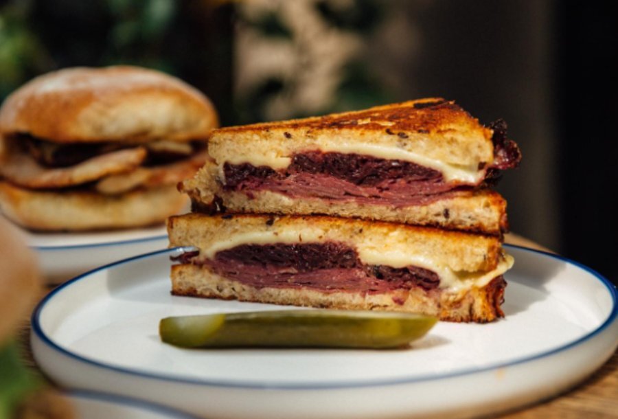 A sliced Reuben toastie on a cafe plate with a pickle. 