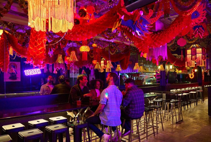 A group of friends in a bar with colourful decorations on the ceiling.